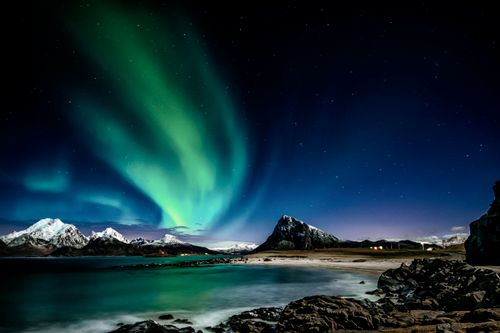 Free Captivating view of the northern lights illuminating a rocky shore and snowy peaks in Nordland, Norway. Stock Photo