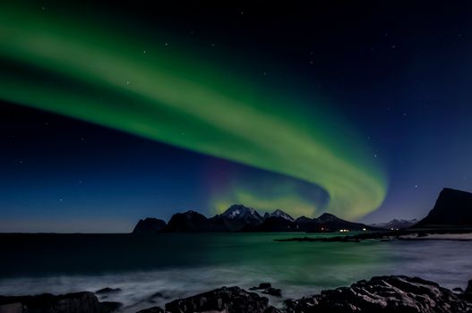 Vibrant aurora borealis illuminating the night sky over Nordland's picturesque rocky shore.