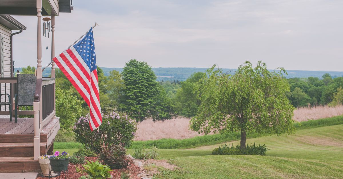 A serene suburban house porch displaying an American flag with a scenic background.