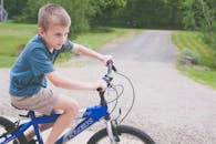阳光明媚的日子里，一个小男孩骑着自行车，沿着绿树环绕的砾石小路前行