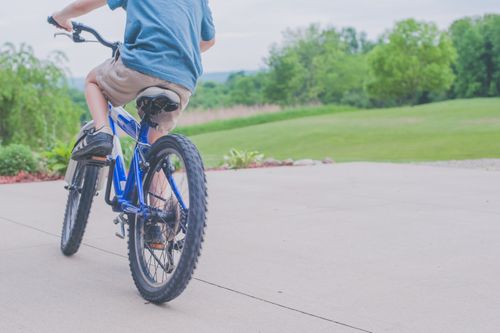 Free A young boy enjoying a ride on a blue bicycle in a lush outdoor setting. Stock Photo
