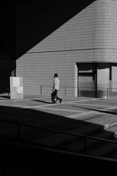 Free Grayscale Photo of Man Walking Near Building  Stock Photo