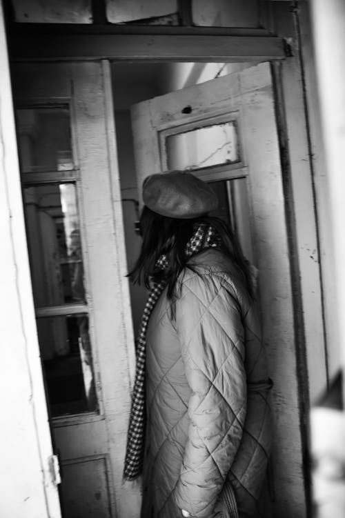 Monochrome Photo of a Person Wearing a Winter Jacket Opening the Door