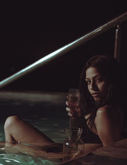 Free A woman in a bathing suit enjoys a drink by the pool under the night sky. Stock Photo
