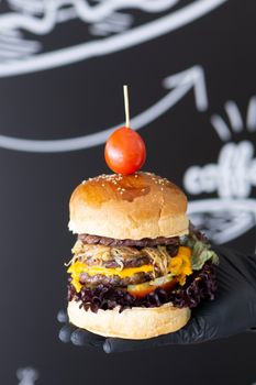 Close-up of a gourmet cheeseburger with a tomato on top, held by a gloved hand.