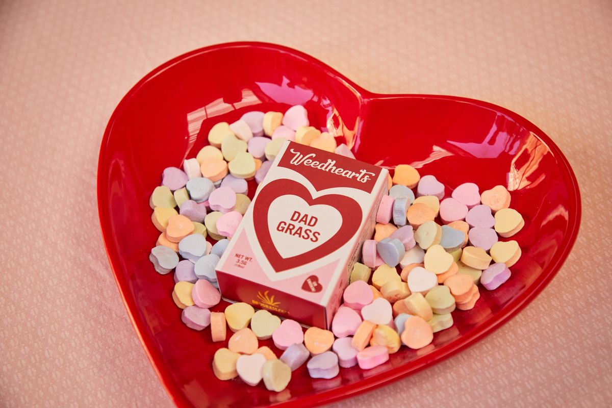 Colorful heart-shaped candies in a red bowl with a Weedhearts box on a pink background.