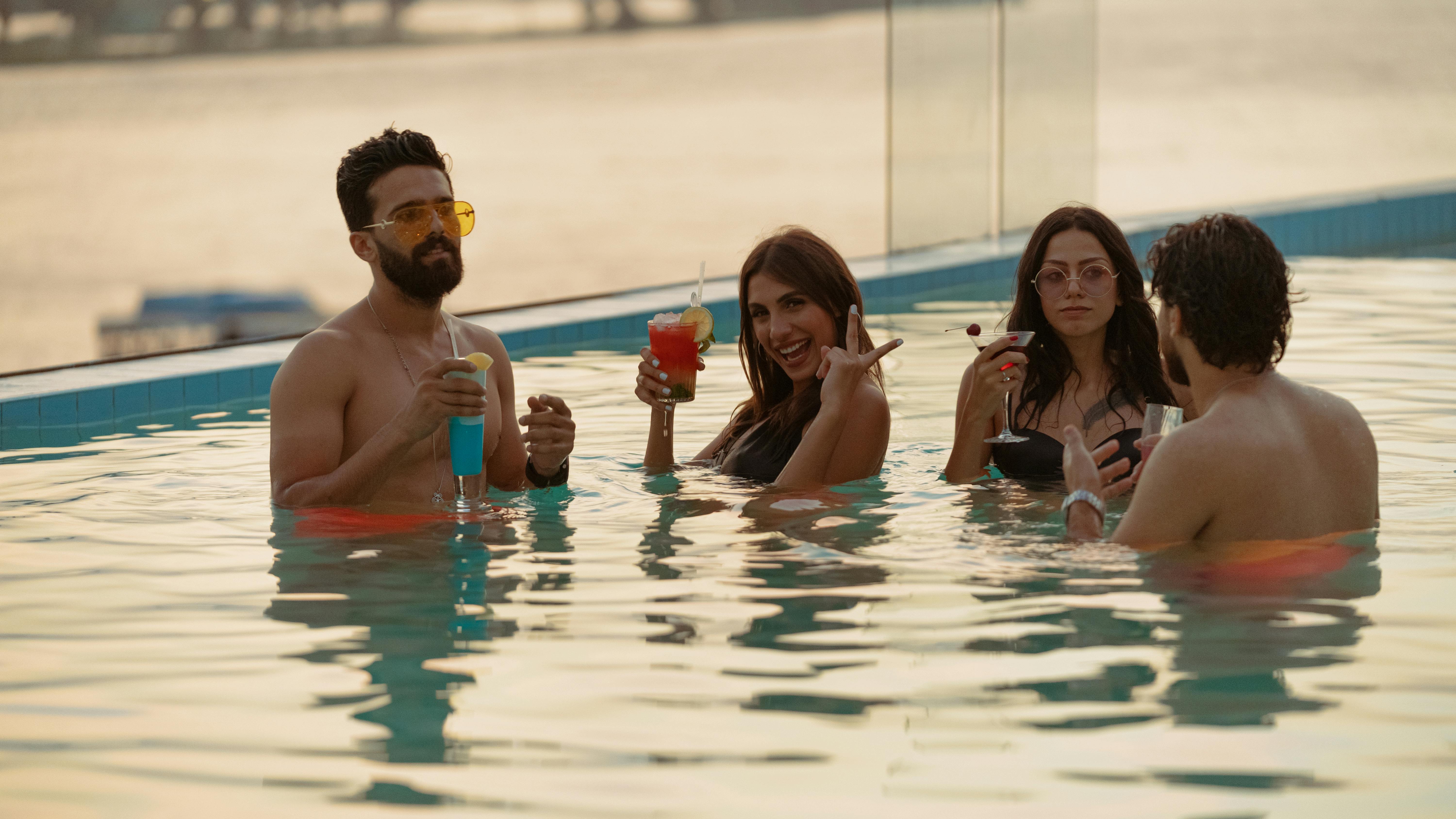 Group of adults relaxing and enjoying cocktails at a rooftop pool party.