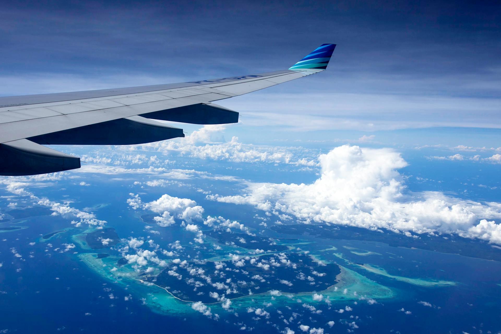Scenic aerial view of ocean and islands through airplane window, highlighting wing and sky.