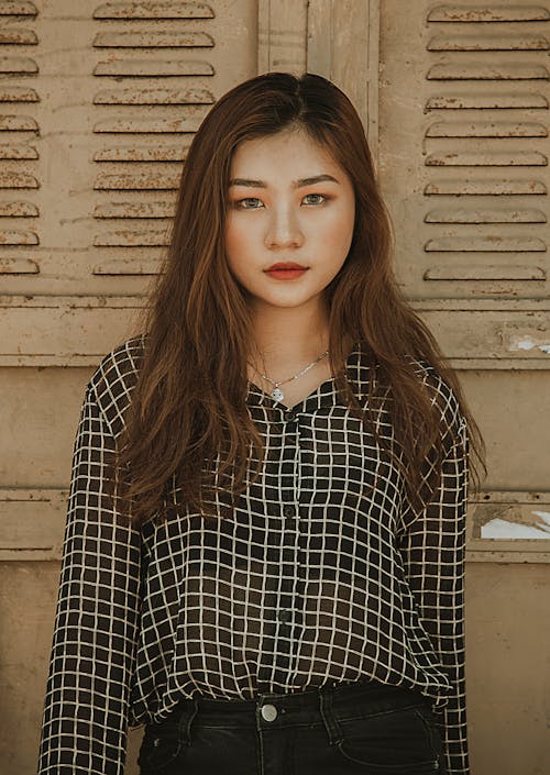 Woman Wearing White and Black Tattersall Collared Button-up Blouse Standing Near Brown Wall