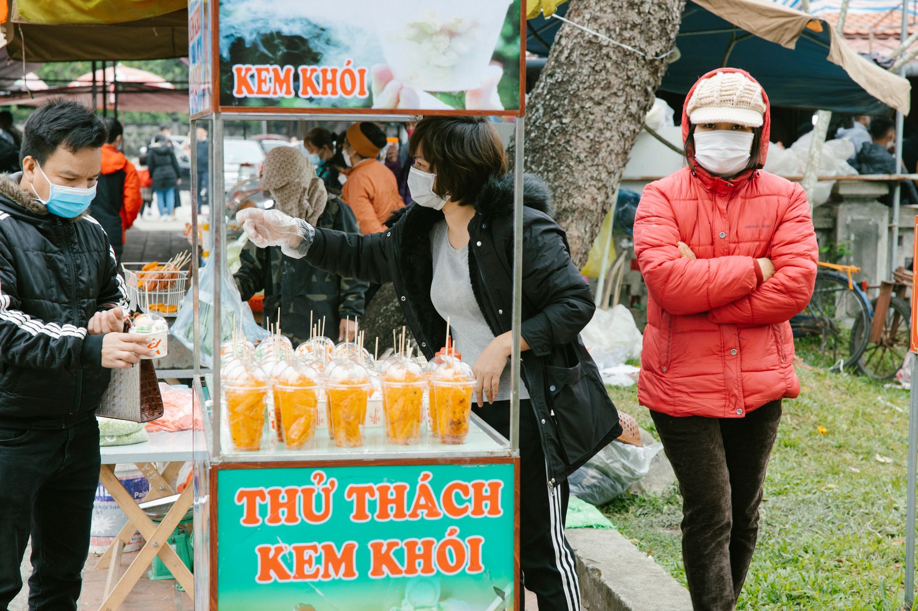 People buying snacks at an outdoor food stand in Hà Nam, Vietnam street market.