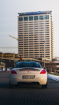 A stylish Peugeot sportscar parked on a city street with a modern skyscraper in the background.