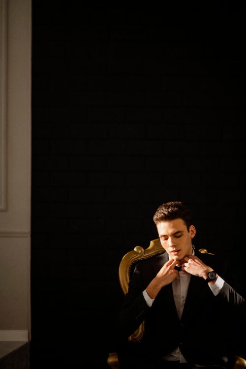 Free Sophisticated portrait of a man adjusting his suit in a classic chair against a dark background. Stock Photo