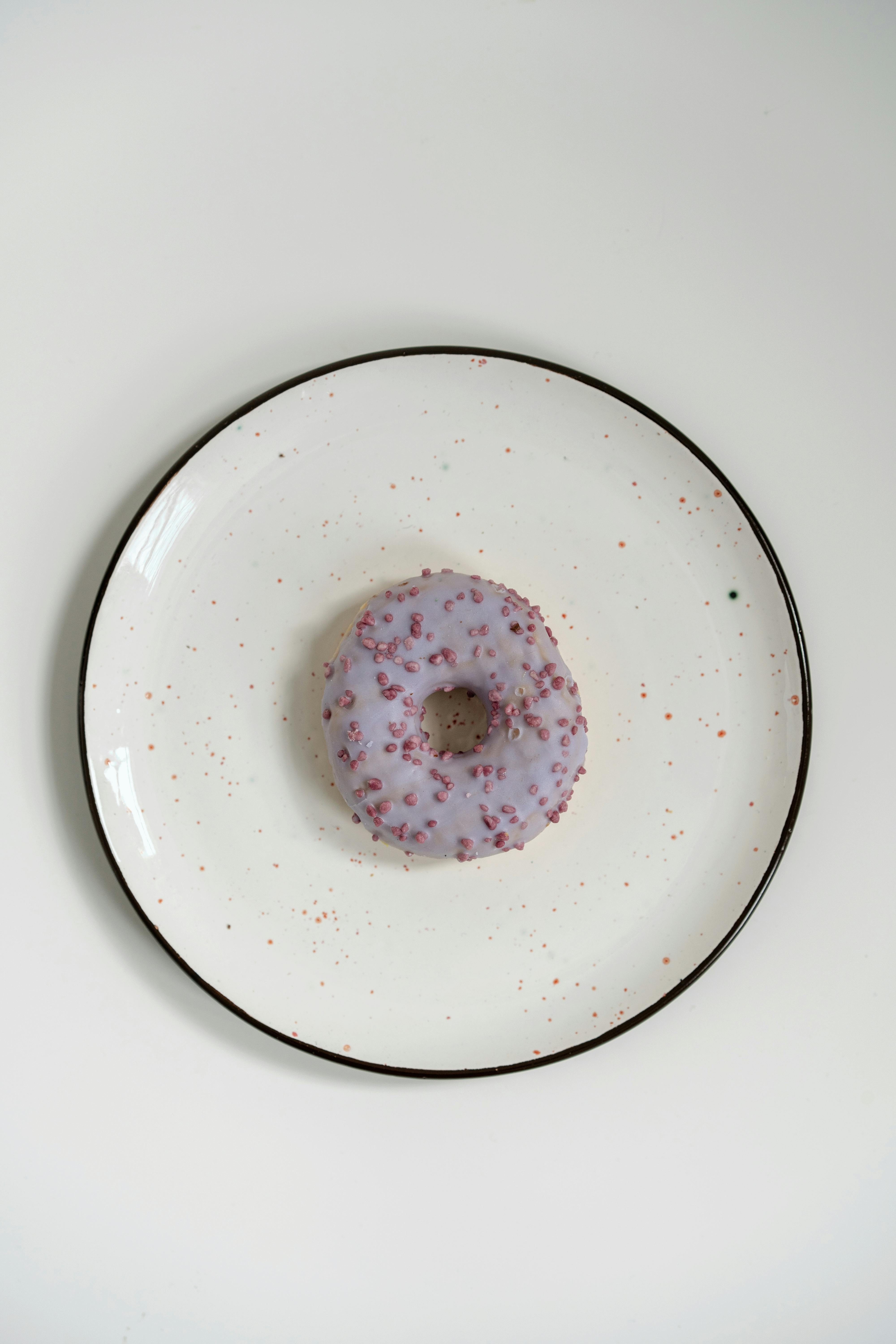 Top view of a single purple iced doughnut on a speckled white plate, showcasing minimalist food art.