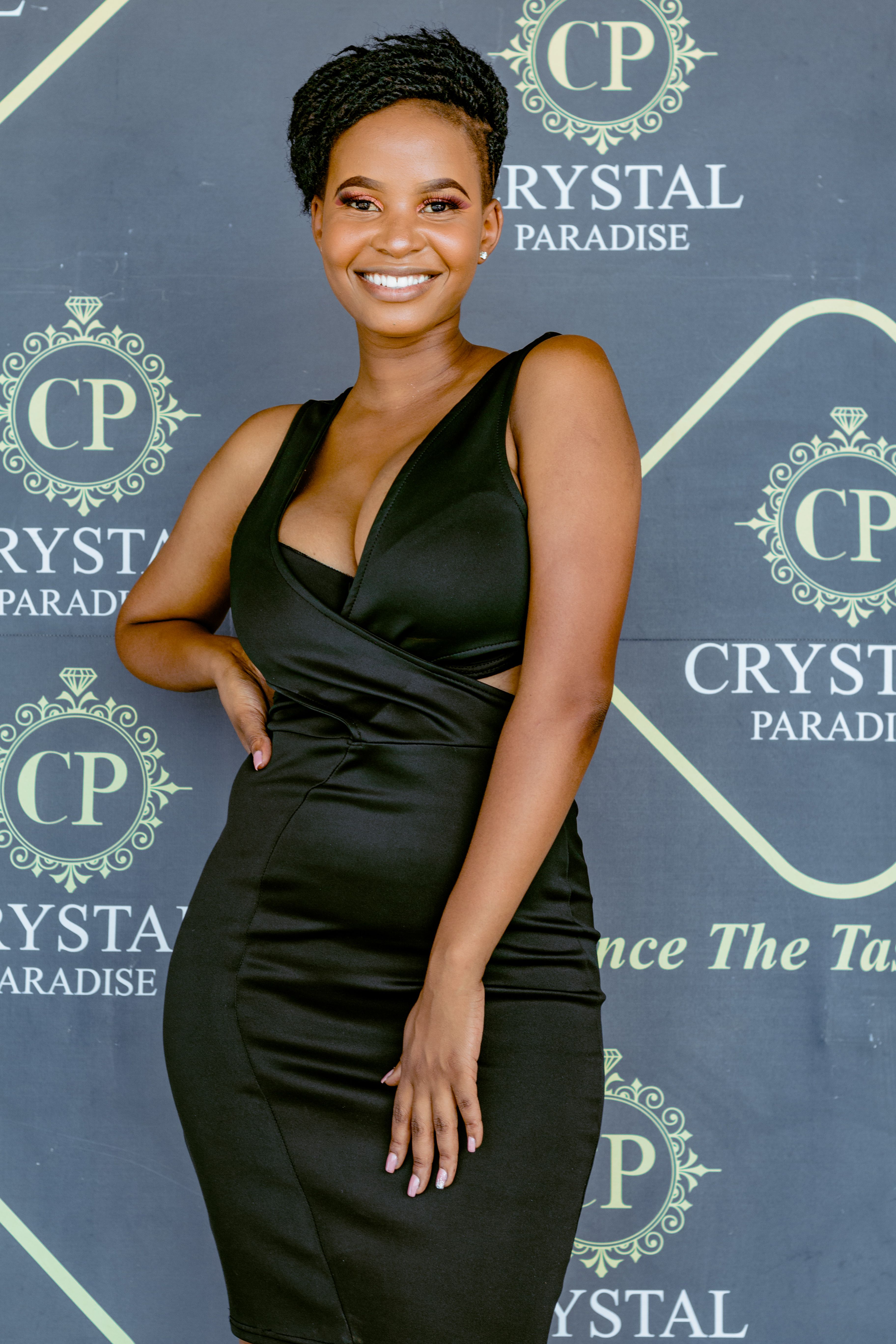 Stylish woman in a black dress poses gracefully at a Crystal Paradise event backdrop.