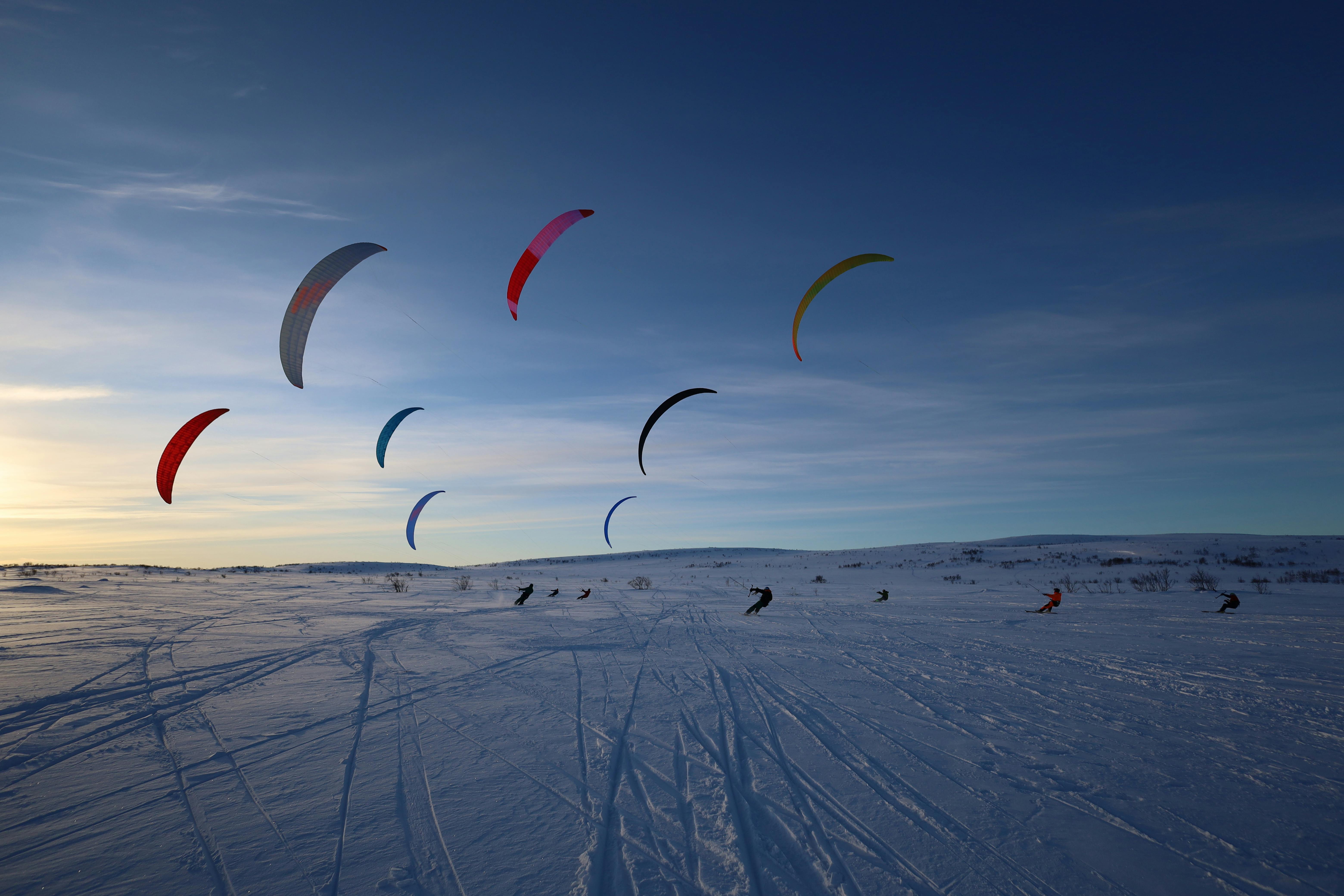 Prescription Goggle Inserts - Colorful snowkiting enthusiasts glide across a vast winter landscape, capturing the thrill of the sport.