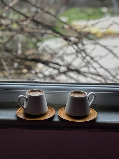 A Cups of Coffee on a Wooden Coasters Near the Glass Window