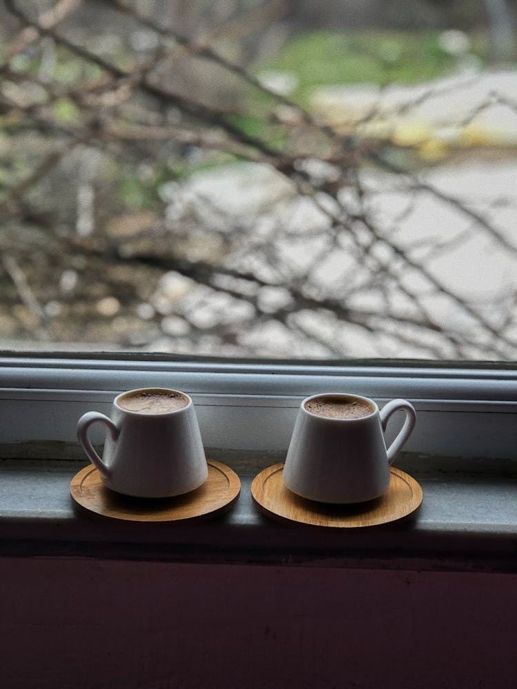 A Cups Of Coffee On A Wooden Coasters Near The Glass Window