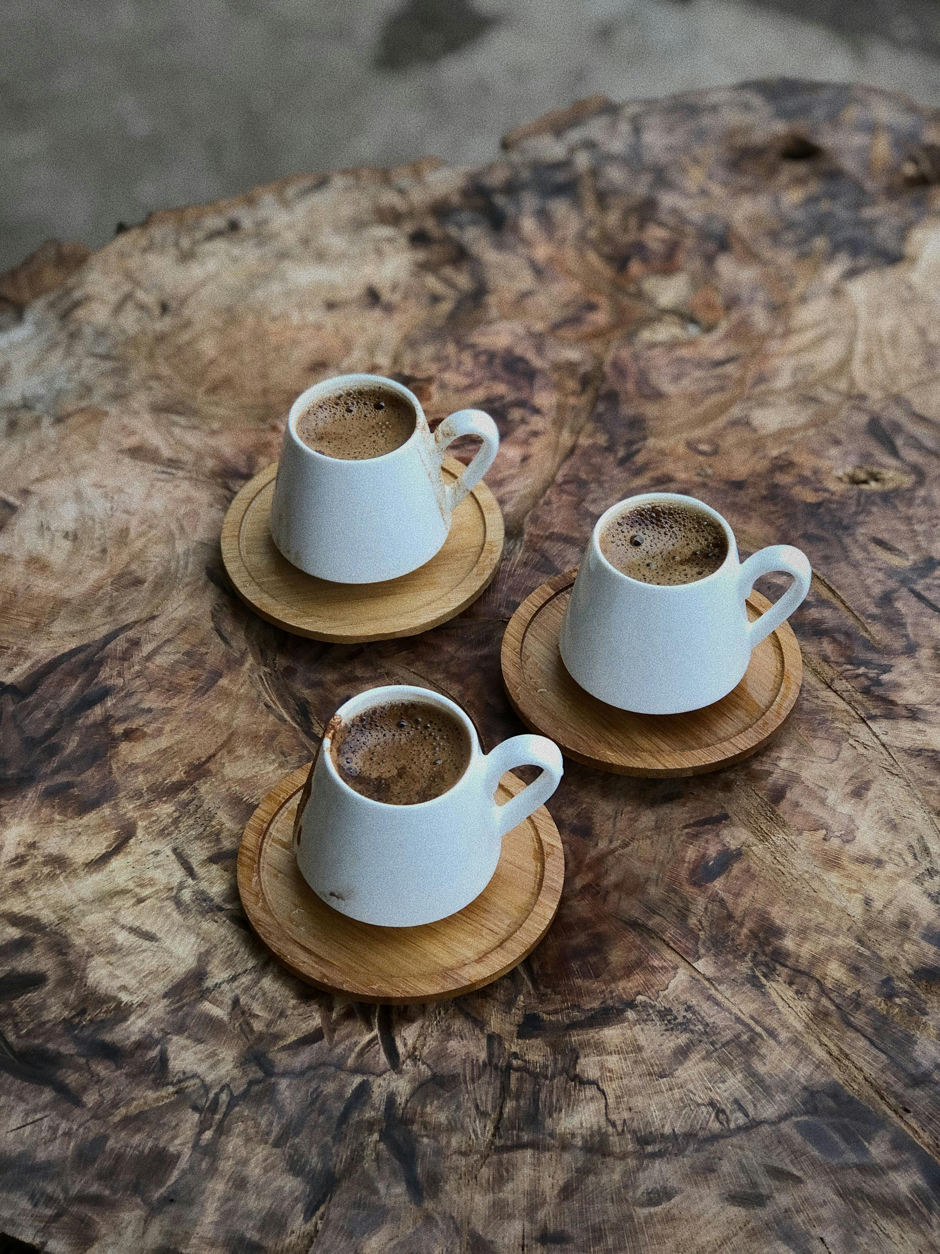 Three white coffee cups on coasters rest on a rustic wooden surface, creating a warm and inviting scene.