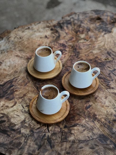 Three white coffee cups on coasters rest on a rustic wooden surface, creating a warm and inviting scene.