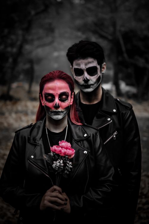 Free Dramatic portrait of two individuals with painted skull faces holding flowers in a spooky setting. Stock Photo