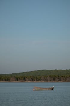 Lone boat floating on a tranquil lake under a clear blue sky, perfect for serene wallpaper settings.