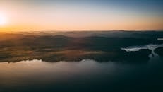 日出时分，薄雾笼罩的山脉与湖泊在鸟瞰中显得宁静祥和，大自然的美丽被尽收眼底