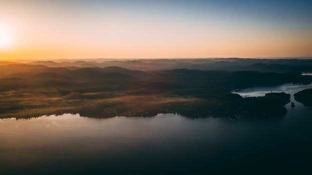 日出时分，薄雾笼罩的山脉与湖泊在鸟瞰中显得宁静祥和，大自然的美丽被尽收眼底