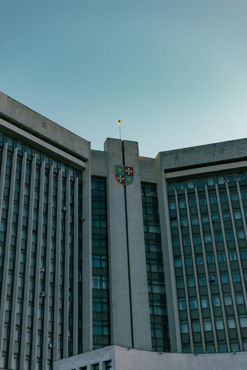 Free Low angle view of a modern government building with a flag and emblem on a clear day. Stock Photo