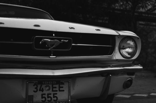 Free Grayscale image of a classic 1965 Ford Mustang with focus on the car's front grille and emblem. Stock Photo