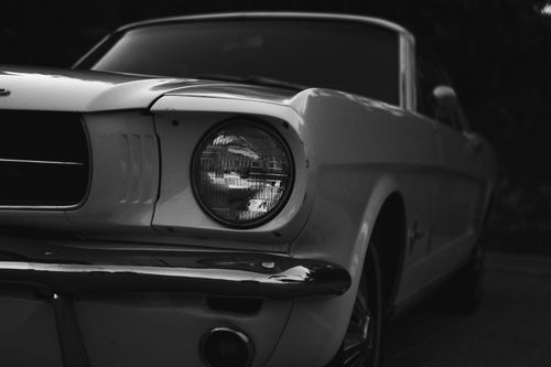 Free Grayscale close-up of a vintage Ford Mustang, showcasing its classic design and iconic headlights. Stock Photo