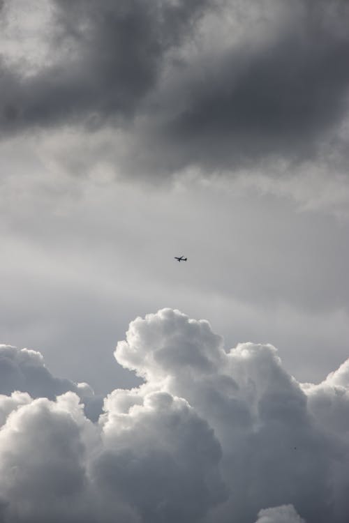 Grayscale Photo of an Airplane Flying in a Cloudy Sky
