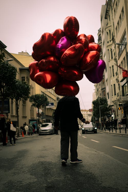 Person Standing in the Middle of the Street Holding Heart Shaped Balloons