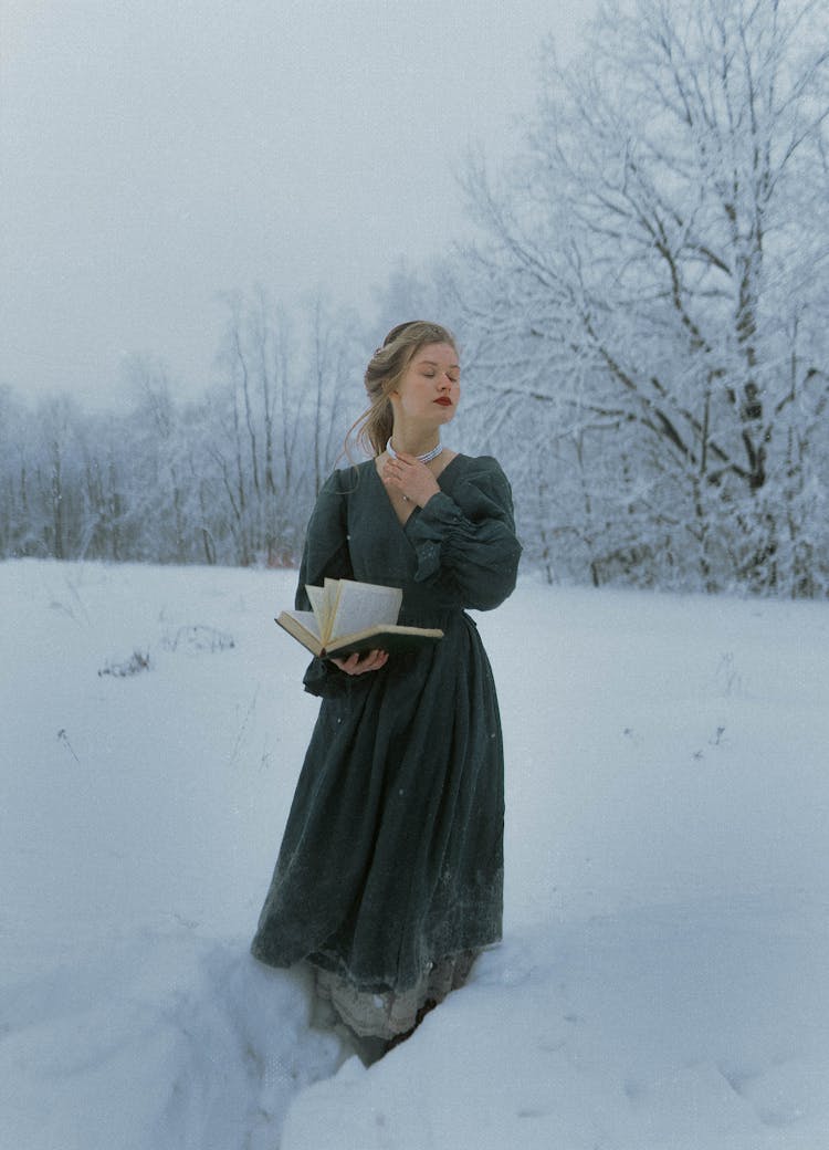 Woman Holding A Book While Standing In Snow 