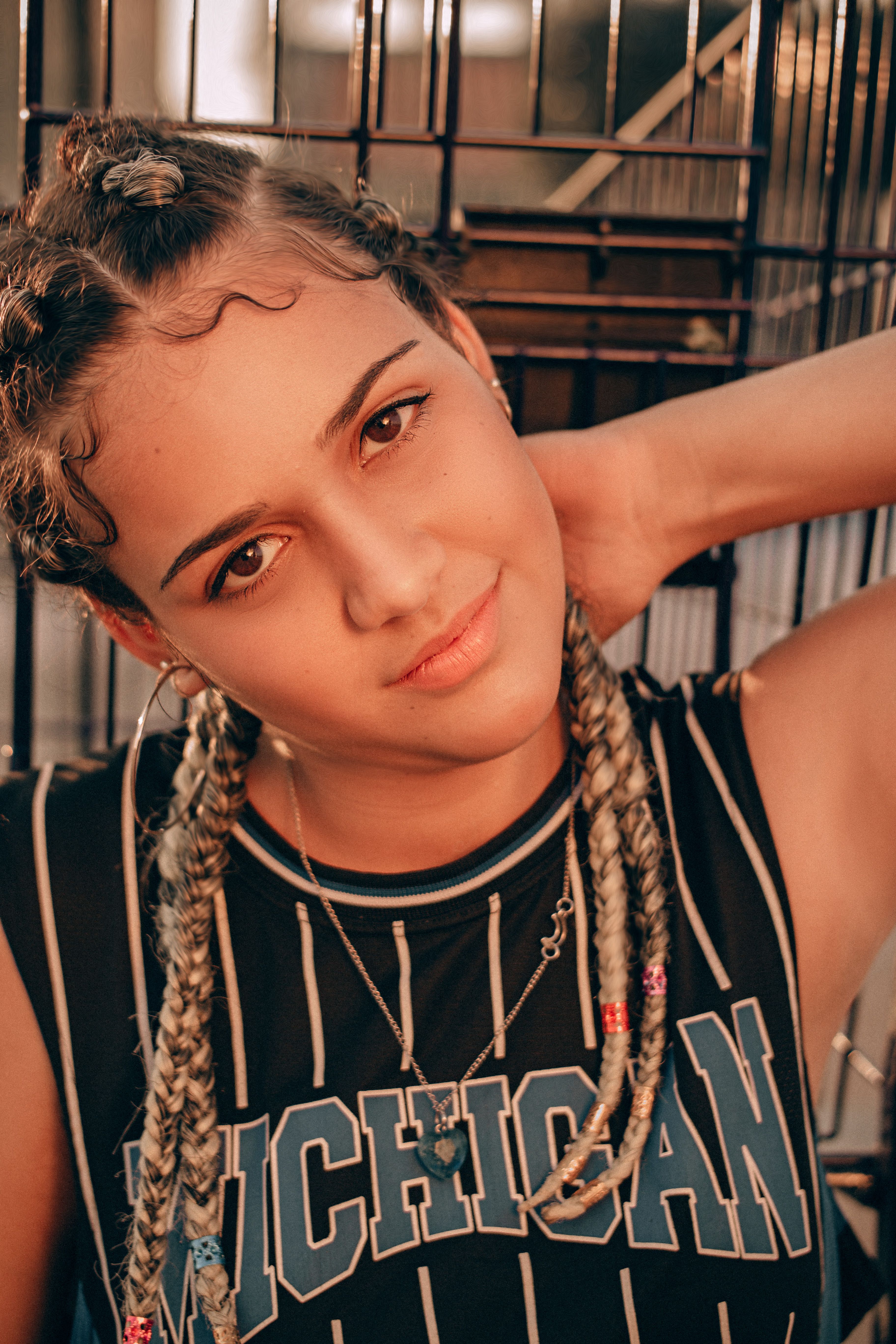 A relaxed portrait of a woman with braided hair and sporty attire in warm lighting.