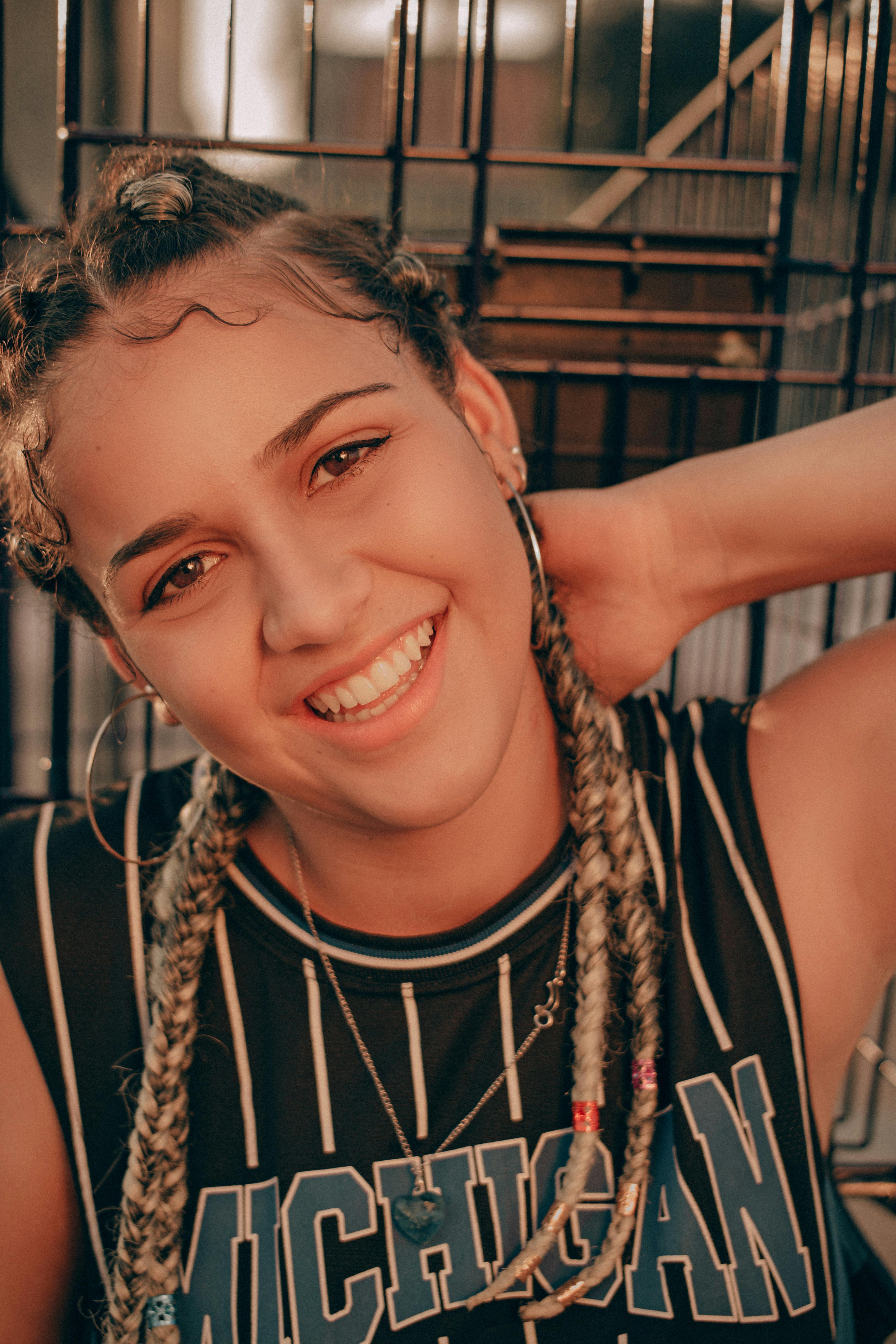 Portrait of a smiling woman with braided hair and hoop earrings, exuding joy and style.