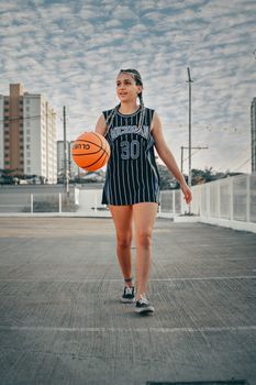 A young woman in a striped jersey playing basketball in an urban setting.