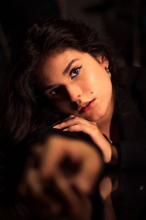 Free A young woman with a pensive expression rests her hand on her cheek in a dramatic portrait. Stock Photo