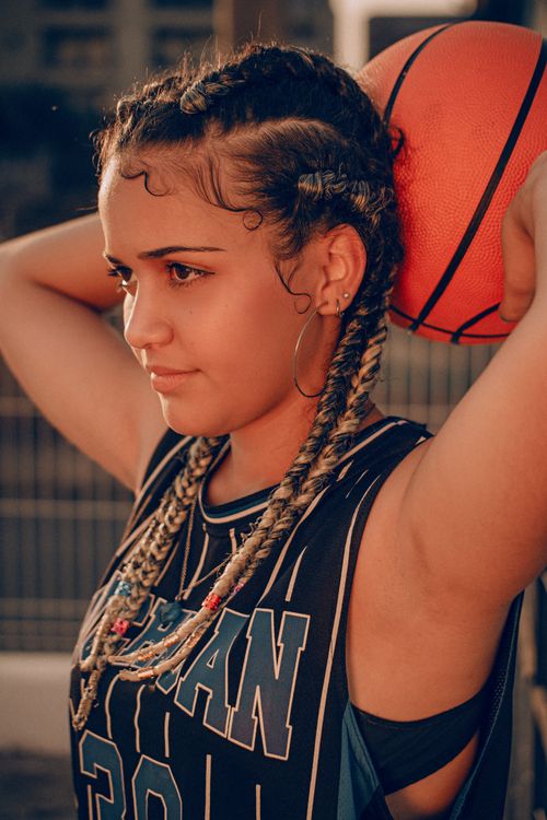 Free Focused young woman with braids and hoop earrings holding basketball, outdoor sportswear fashion. Stock Photo