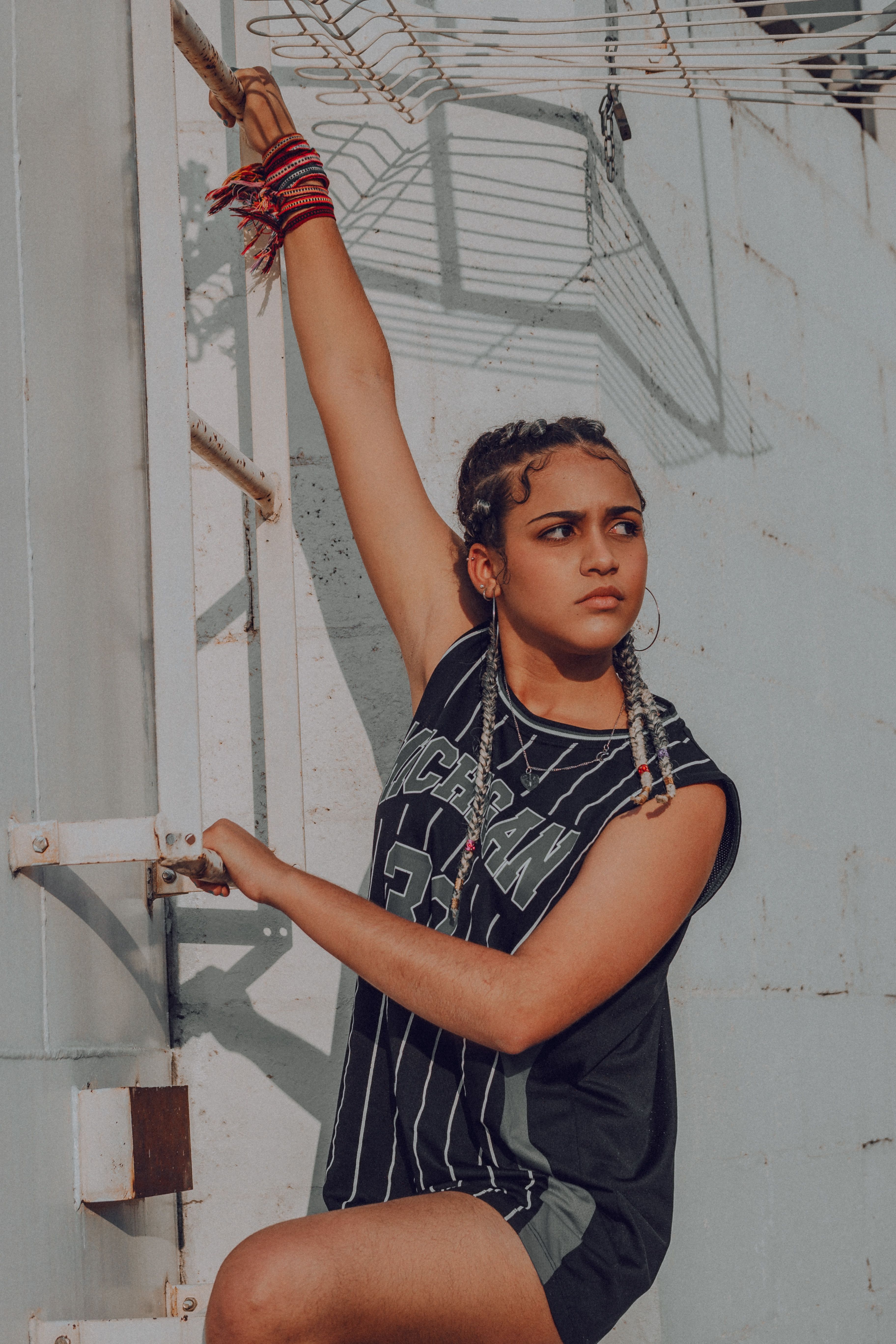 Confident young woman climbing a metal structure outdoors with braided hair and sporty jersey.