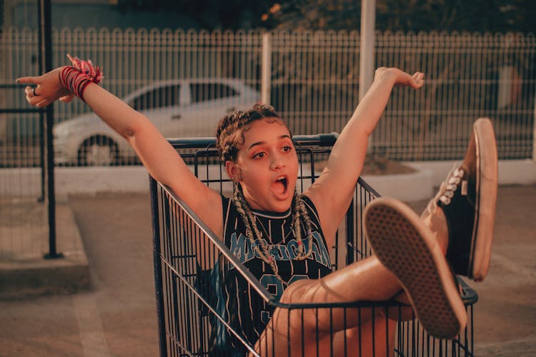 Photo Of A Teenage Girl Sitting In A Shopping Cart On A Car Park