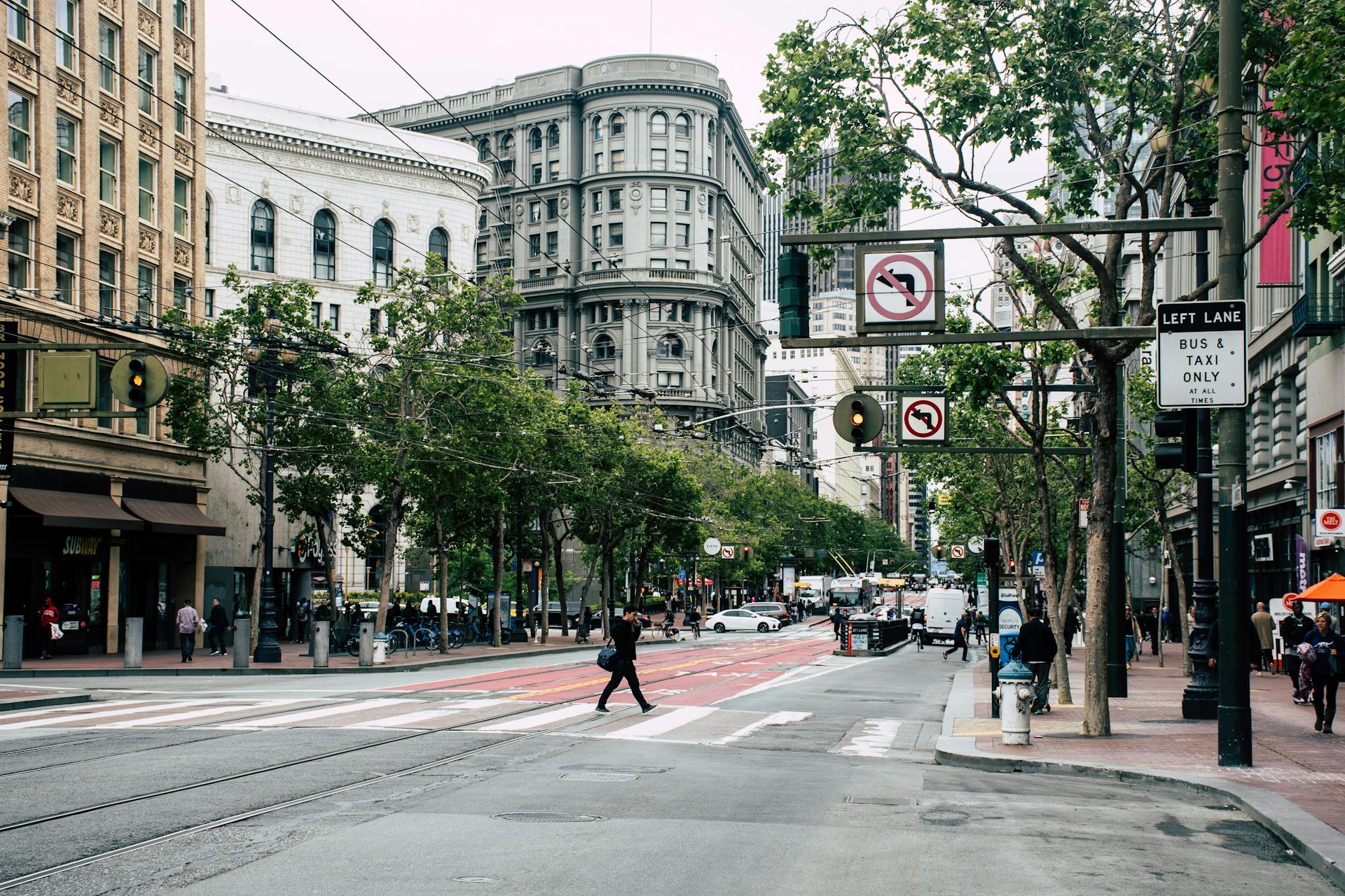 A bustling downtown San Francisco street with historic buildings and pedestrians crossing.