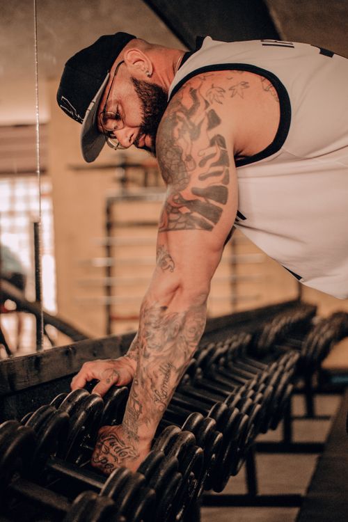 Free Muscular man with tattoos works out in a gym, emphasizing fitness and strength. Stock Photo