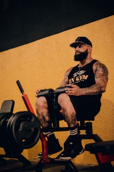 Bearded, muscular man in a black tank top exercising at the gym.