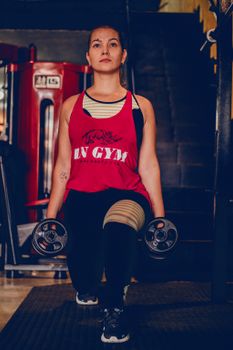 Focused woman performing lunges with dumbbells in a modern gym setting.