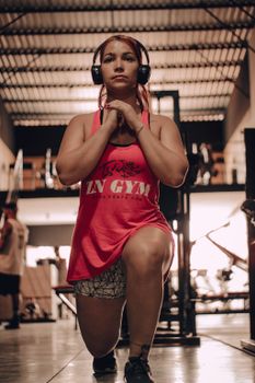 Woman in pink tank top performing lunge exercise indoors in gym setting.