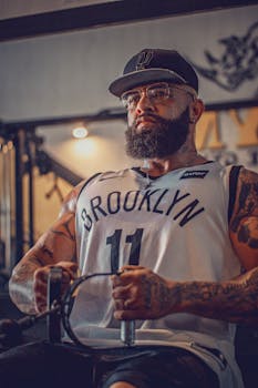 Bearded man with tattoos working out indoors in gym, emphasizing fitness and strength.