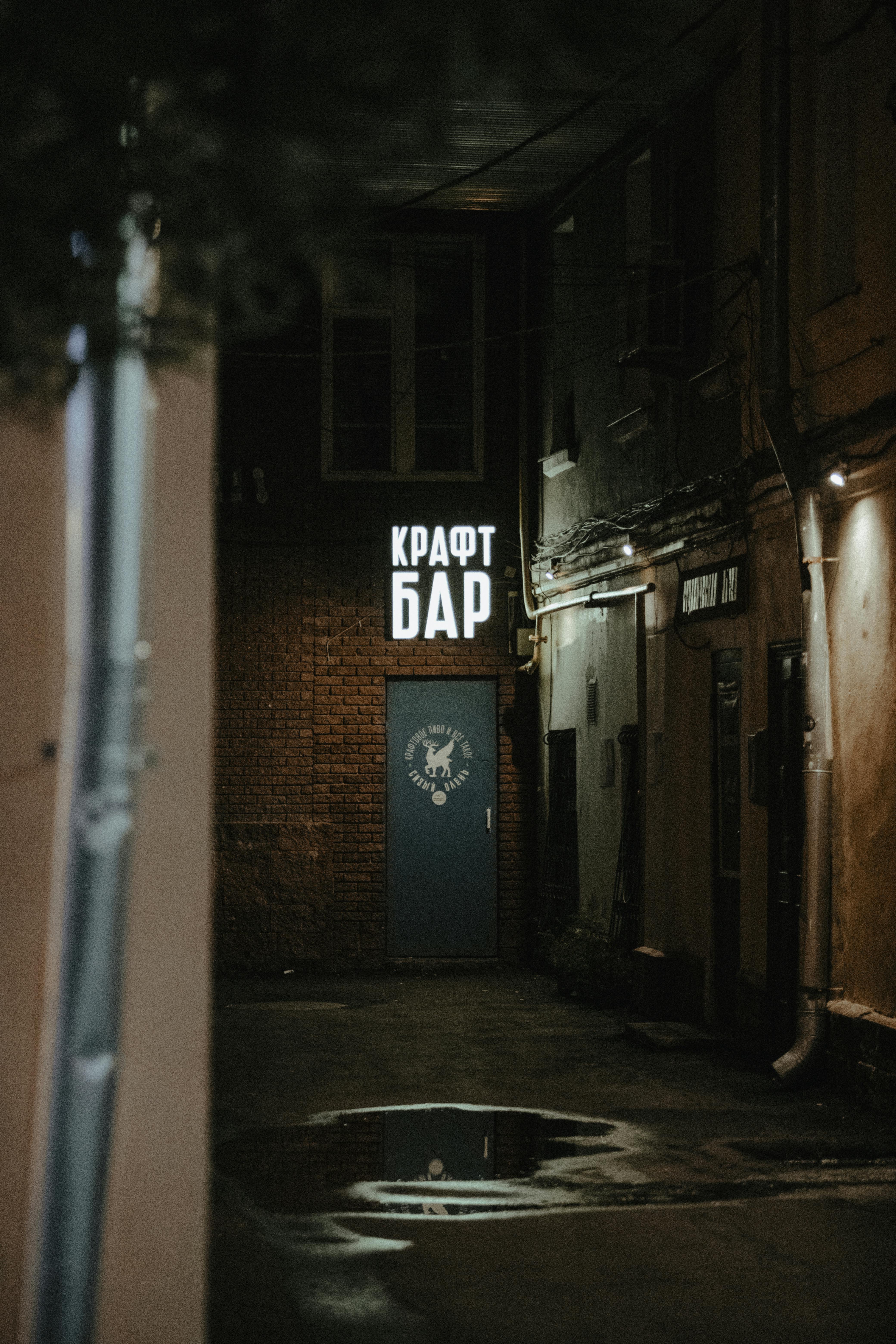 Dark alley featuring illuminated neon signage leading to a craft bar, evoking a mysterious urban atmosphere.