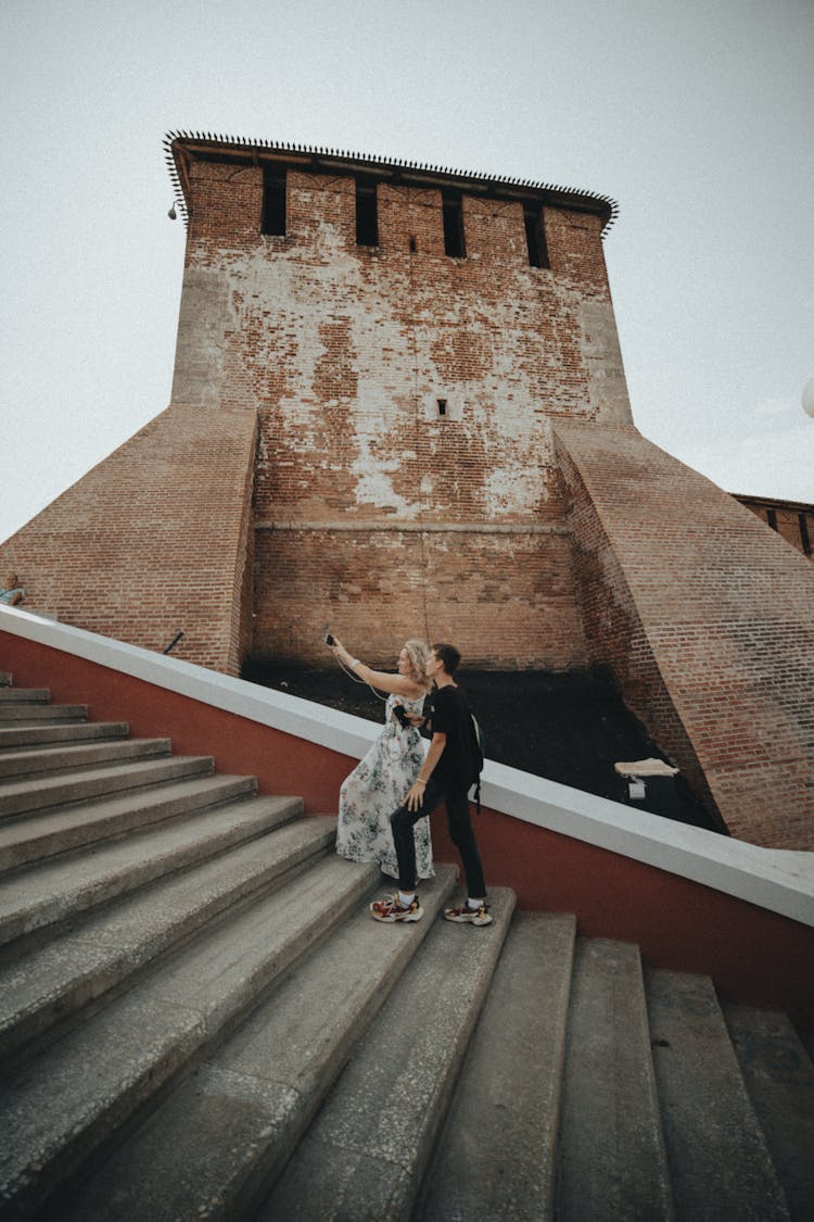 Young Couple Making Selfie On Stairs With Old Building As Background