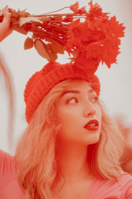 Stylish young woman in a red hat poses with red flowers, exuding elegance and charm.
