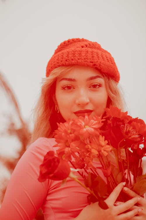 A Woman in Red Knit Cap Holding Red Flowers